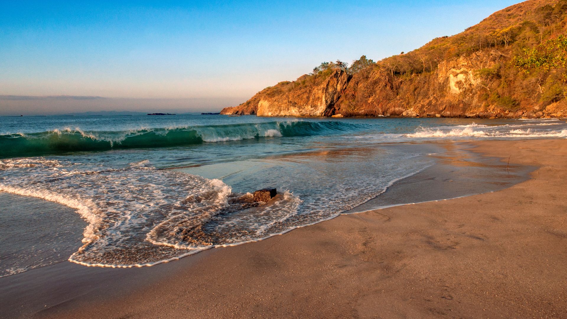 Sandy beach with gentle waves and rocky cliffs under a clear blue sky, embodying the serene beauty of Costa Rica's Pacific side.